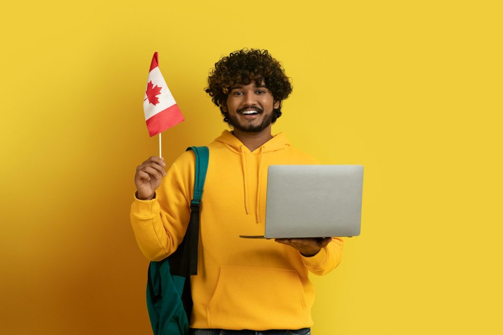 Smiling indian man holding laptop and flag of Canada